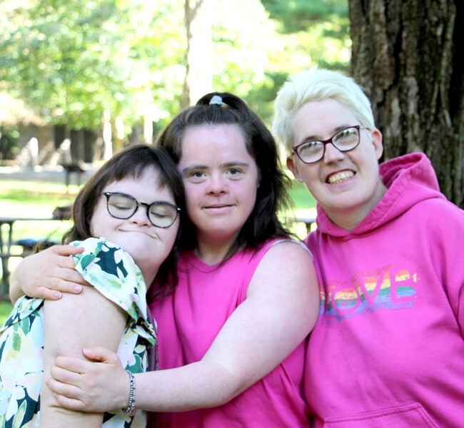 Three smiling women in pink shirts and glasses embrace each other in a cheerful hug. Three smiling women in pink shirts and glasses embrace each other in a cheerful hug.
