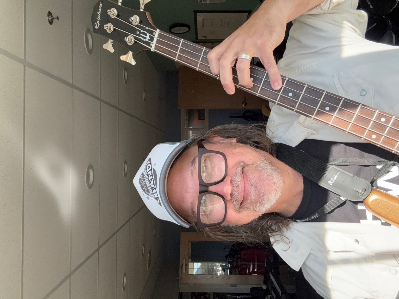 Eddy, a white man with long hair, is wearing a white baseball cap and holding a guitar.