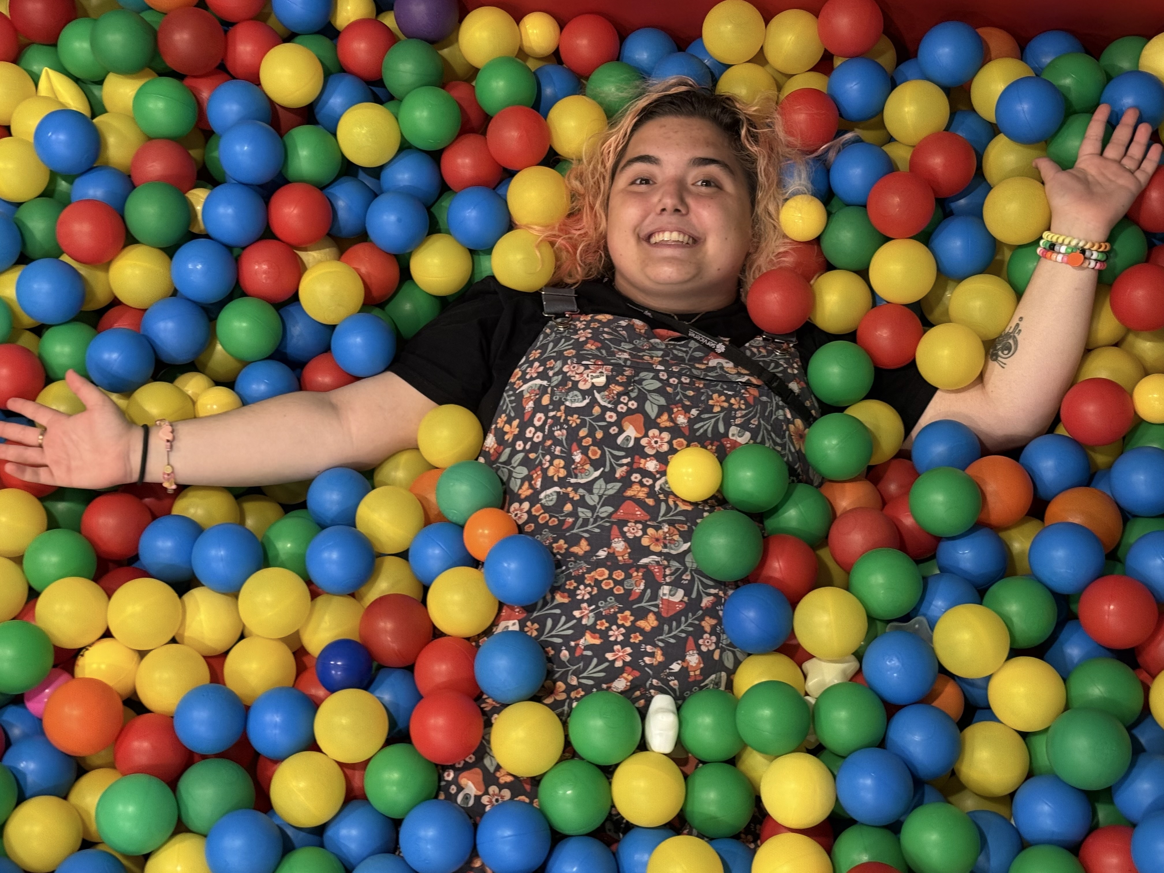 Ella is wearing a jumper and black tshirt, smiling at the camera from the ball pit.